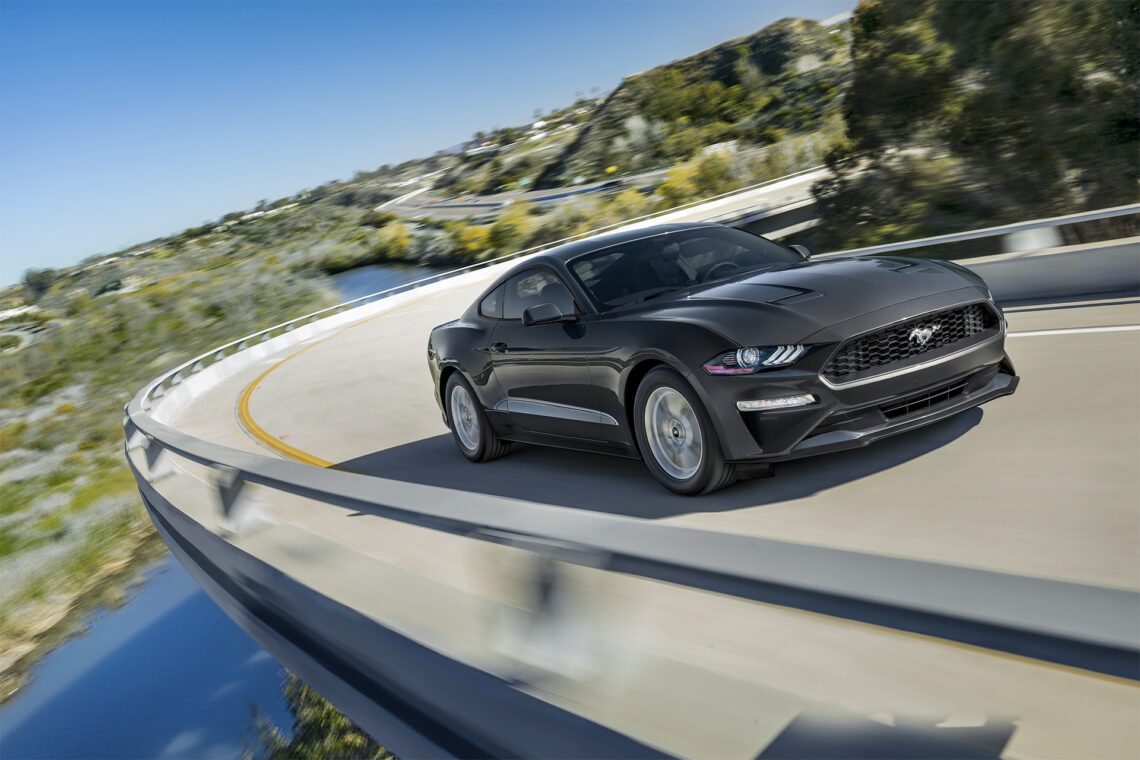 A black 2023 Ford Mustang taking a curve overlooking the wilderness